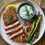 Baked Tuna Steak Recipe: The Best 25-Minute Healthy Dinner 11 Tuna steak served with roasted asparagus, onions, lemon wedge, and yogurt sauce on a white plate.