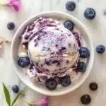 Blueberry Cheesecake Ice Cream Recipe: Irresistibly Creamy & Easy to Make 8 Top-down view of a scoop of blueberry cheesecake ice cream with marbled blueberry swirls, served in a pastel dessert bowl.