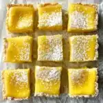 Gluten Free Lemon Bars Recipe – The Best Zesty Treat 7 Gluten free lemon bars topped with powdered sugar on parchment paper